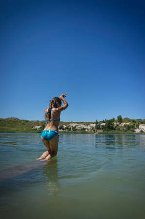 A little cute girl in a swimsuit jumps into the blue water of a career lake.の写真素材