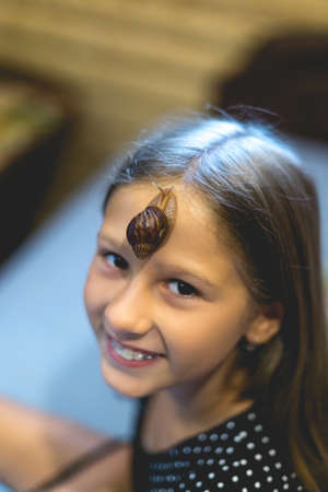 Little Achatina snail on the forehead of a cute little girlの写真素材