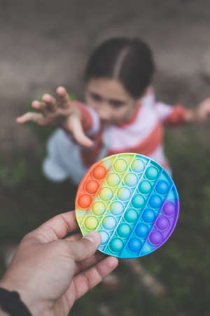 A little cute girl is trying to take away from her father a silicone toy-antistress pop itの写真素材