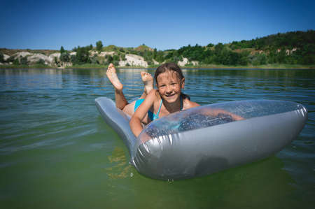 A little cute girl in a swimsuit swims on an inflatable mattress on a blue career lake.の写真素材