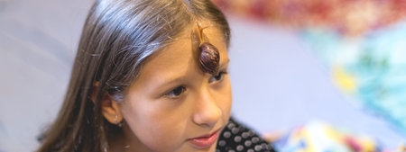Little Achatina snail on the forehead of a cute little girlの写真素材