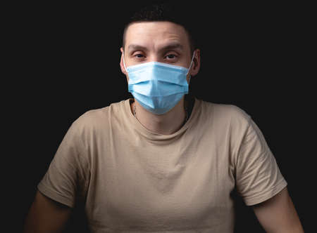 Handsome young man in medical mask over isolated black background. Studio photo with one light sourceの写真素材