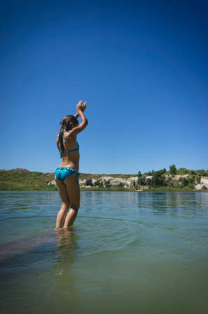 A little cute girl in a swimsuit jumps into the blue water of a career lake.の写真素材