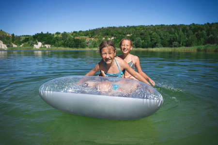 Two little cute girls in swimsuits swim on an inflatable mattress on a blue career lake.の写真素材