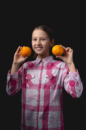 Little cute girl posing with tangerines in the studio. Photo isolated on black background with one light source. The child is holding a pair of tangerines to his face.の写真素材