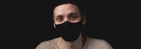 Handsome young man in medical mask over isolated black background. Studio photo with one light sourceの写真素材