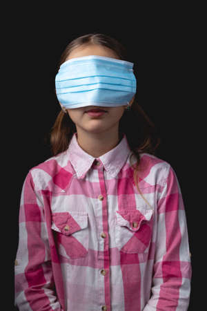 Little girl with a blue medical mask. The concept of wearing a medical mask incorrectly. Studio portrait isolated on black background with one light sourceの写真素材