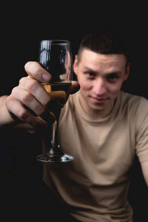 Handsome young man with glass of champagne over isolated black background. Studio portrait with one light sourceの写真素材
