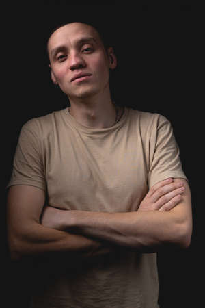 Handsome young man posing over black background. Studio photo with one light source. The guy is standing with his arms crossed over his chest.の写真素材