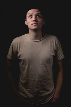 Handsome young man posing over black background. Studio photo with one light source. Guy praying looking up.の写真素材
