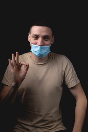 Handsome young man and a medical mask on a black background. The man shows how wrong it is to wear a medical mask.の写真素材