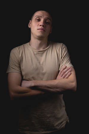 Handsome young man posing over black background. Studio photo with one light source. The guy with his head up is standing with his arms crossed over his chest.の写真素材