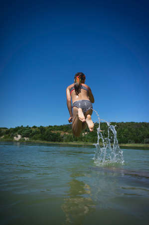 A little cute girl in a swimsuit jumps into the blue water of a career lake.の写真素材
