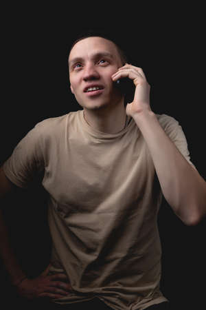 Studio portrait of a man with a smartphone on a black background. Handsome guy talking on the phone. Photo with one light source.の写真素材