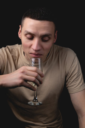 Handsome young man with glass of champagne over isolated black background. Studio portrait with one light sourceの写真素材