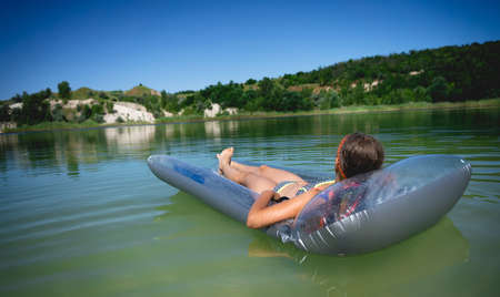 A little cute girl in a swimsuit swims on an inflatable mattress on a blue career lake.の写真素材