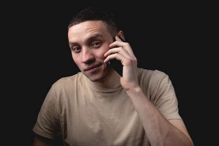 Studio portrait of a man with a smartphone on a black background. Handsome guy talking on the phone. Photo with one light source.の写真素材