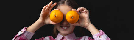 Little cute girl posing with tangerines in the studio. Photo isolated on black background with one light source. The child is fooling around closing his eyes with tangerines.の写真素材