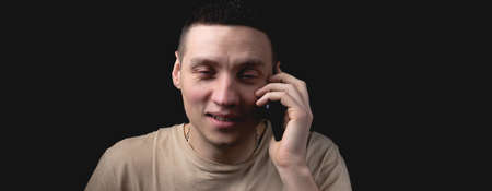 Studio portrait of a man with a smartphone on a black background. Handsome guy talking on the phone. Photo with one light source.の写真素材