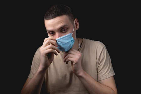 Handsome young man and medical mask over isolated black background. The man puts on a medical mask. Studio photo with one light sourceの写真素材
