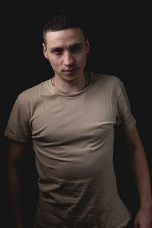 Handsome young man posing over black background. Studio photo with one light source. The guy straightened his shoulders and looks intimidating in front of him.の写真素材