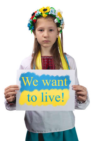 A little Ukrainian girl with tears in her eyes holds a sheet of paper with the inscription "We want to live!" in her hands. Studio photo on a white background.の写真素材