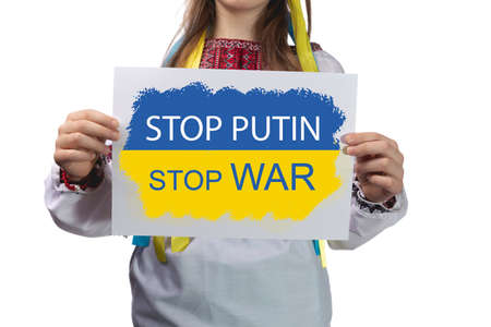 A little Ukrainian girl holds a sheet of paper with the inscription "Stop putin stop war" in her hands. Studio photo on a white background.の写真素材