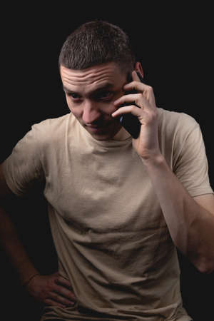 Studio portrait of a man with a smartphone on a black background. Handsome guy talking on the phone. Photo with one light source.の写真素材