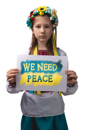 A little Ukrainian girl with tears in her eyes holds a sheet of paper with the inscription "We need peace" in her hands. Studio photo on a white background.の写真素材