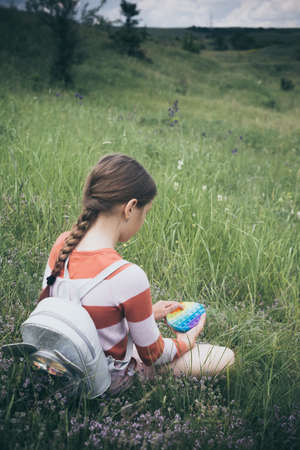 A little cute girl is sitting on the grass with antistress toy.の写真素材
