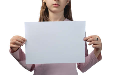 Little cute Ukrainian girl 11 years old posing in the studio on a white background. The child holds a blank white sheet in his hands. Preparation for the inscription. Studio photo isolated on white background.の写真素材