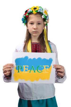 A little Ukrainian girl with tears in her eyes holds a sheet of paper with the inscription "Peace" in her hands. Studio photo on a white background.の写真素材