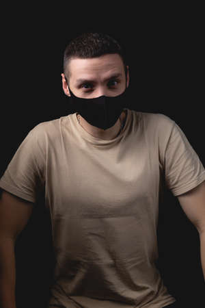 Handsome young man in medical mask over isolated black background. Studio photo with one light sourceの写真素材