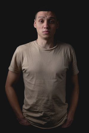 Handsome young man posing over black background. Studio photo with one light source. Smiling guy cheerfully posing in the studio. The guy looks in front of him indignantly.の写真素材