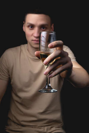 Handsome young man with glass of champagne over isolated black background. Studio portrait with one light sourceの写真素材