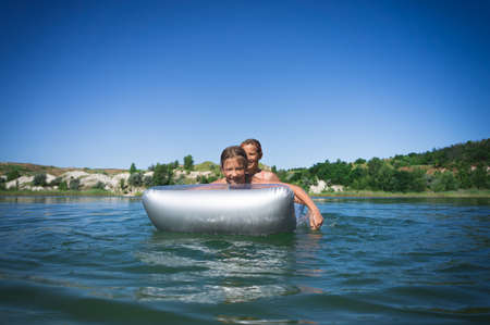 Two little cute girls in swimsuits swim on an inflatable mattress on a blue career lake.の写真素材