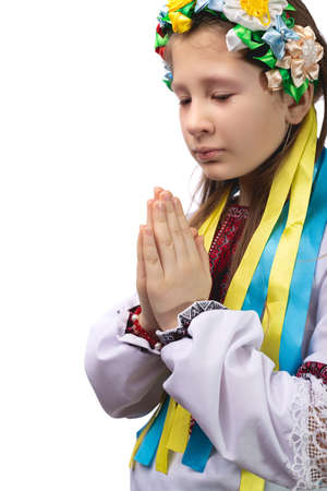 A little girl in national Ukrainian clothes with tearful eyes folded her hands in front of her and prays for an end to the war in Ukraine. Studio photo on a white background.の写真素材