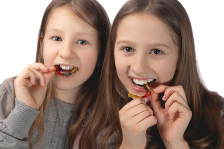 Two cute girls playfully pose with orthodontic appliances in their hands on a white background. The concept of oral hygiene in childhood. studio photo.の写真素材