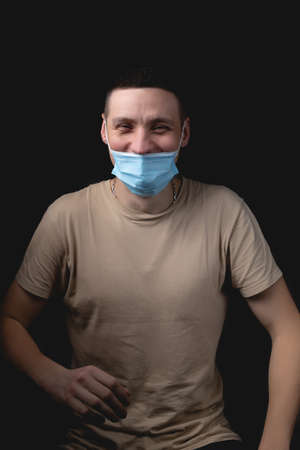 Handsome young man and a medical mask on a black background. The man shows how wrong it is to wear a medical mask.の写真素材