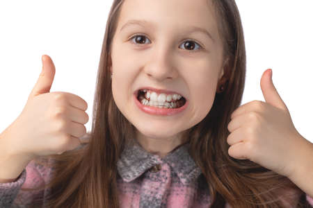 Cute little girl with orthodontic appliance showing thumbs up. The concept of oral hygiene in childhood. Studio photo on a white background.の写真素材