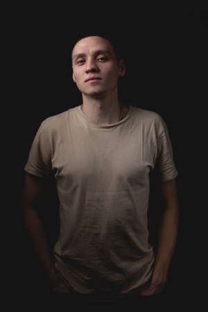 Handsome young man posing over black background. Studio photo with one light source. The guy looks in front of him approvingly with his hands in his pockets.の写真素材