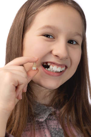 A cute little girl holds a recently removed molar in her hand and shows the place from which this tooth was removed. Studio photo on a white background.の写真素材