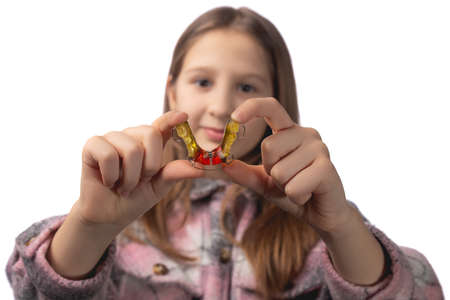 Cute little girl posing in the studio holding an orthodontic appliance in her hand. The concept of oral hygiene in childhood. Photo on a white background.の写真素材