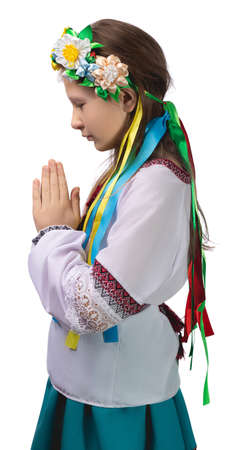 A little girl in national Ukrainian clothes with tearful eyes folded her hands in front of her and prays for an end to the war in Ukraine. Studio photo on a white background.の写真素材