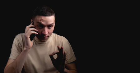 Studio portrait of a man with a smartphone on a black background. Handsome guy talking on the phone. Photo with one light source.の写真素材