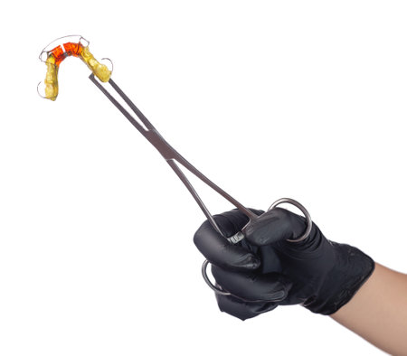 A doctor's hand in a black medical glove holds a colorful children's orthodontic appliance in a clip. The concept of oral hygiene in childhood. Studio photo isolated on white background.の写真素材