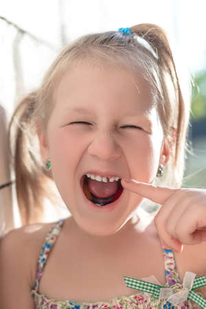 Little girl points the finger at a wobbly baby tooth.の写真素材