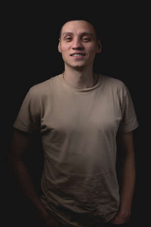 Handsome young man posing over black background. Studio photo with one light source. Smiling guy cheerfully posing in the studio.の写真素材