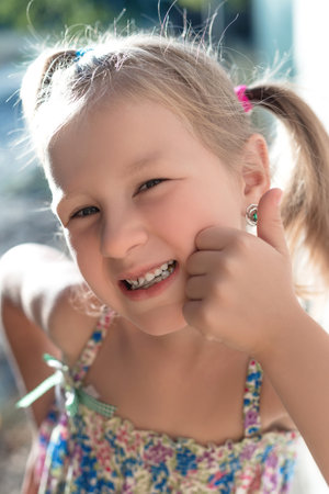 Portrait of a little girl with a wobbly baby tooth and a thumb up.の写真素材
