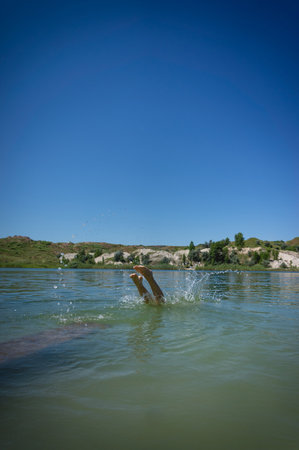 A little cute girl in a swimsuit jumps into the blue water of a career lake.の写真素材